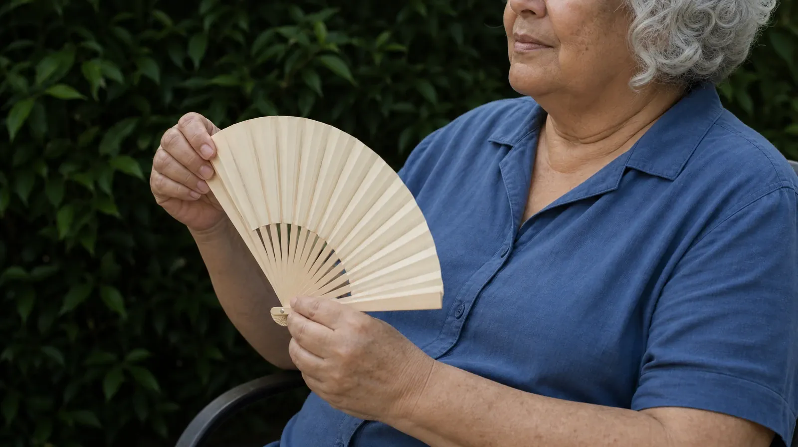 An adult unfolds a plain hand fan while sitting outdoors in the shade · Residential Addiction Treatment for Big Torch Key, FL