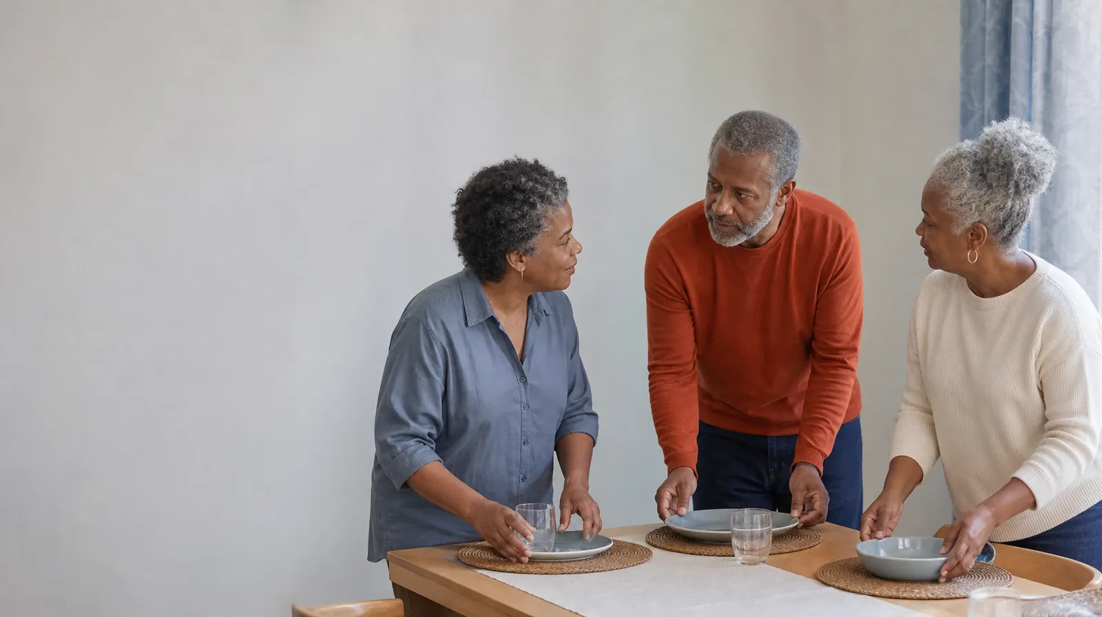 Three adults pause while setting a plain table · Family Involvement and Grief support in South Florida