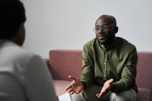 a person with glasses sits on the couch and asks a therapist what is CBT