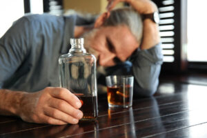older person sitting at bar hanging his head and drinking a bottle of liquor while struggling with the fact that alcoholics do get worse with age