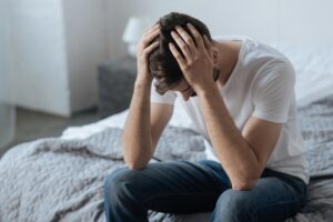 Man rests head in hands while sitting on bed, wondering if kratom is addictive